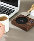 Electric Coffee Mug Warmer With Three Heat Settings And Four Hour Auto Shutoff keeps coffee warm by a laptop on a desk.
