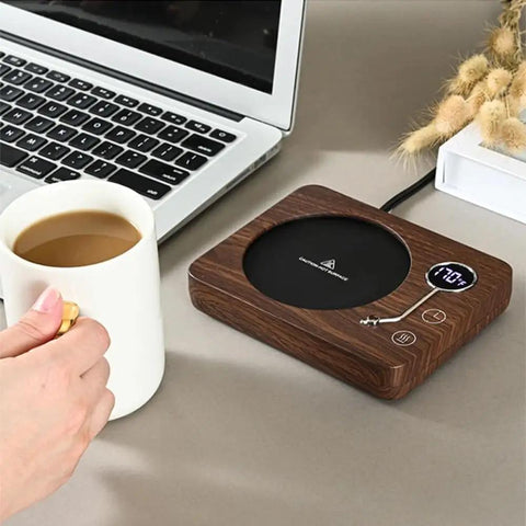 Electric Coffee Mug Warmer With Three Heat Settings And Four Hour Auto Shutoff keeps coffee warm by a laptop on a desk.