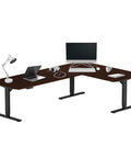 Level Up Your Setup With This Bad Boy Electric L Shaped Standing Desk In Roasted Walnut And Black Frame 83X55 Inch Extra Large Corner Workstation height adjustable with laptop and lamp.