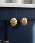 Close-up of champagne bronze floral cabinet knobs installed on blue kitchen cabinets, highlighting vintage round design.