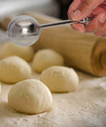 One-handed operation stainless steel flour duster sifter shaking powdered sugar over dough with rolling pin in the background.
