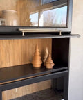 Ponderosa Premium Interior Wood Aging Stain 5 Gallon Container on wooden shelf with decorative trees and glass door.
