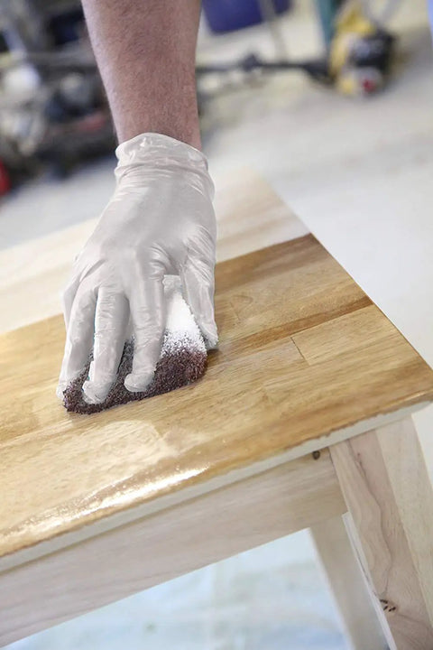 Hand in glove using Super Tuff Staining Pad Set With Free Gloves 12 Pack 4x5 Inch Sponge With White Terry Cloth on wood surface