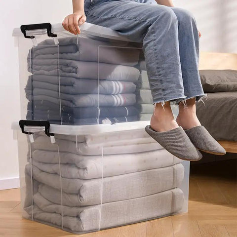 Person sitting on Sleek Clear Plastic Storage Bins With Secure Lids 90 Quarts 8 Pack Heavy Duty, filled with folded blankets.