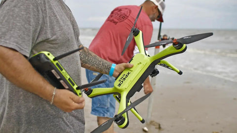 Man holding waterproof fishing drone with 7 pound bait release and 4K camera at the beach, preparing to fly.