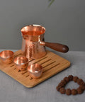 Copper Teapot With Wooden Handle Dope Hammered Turkish Coffee Pot on wooden tray, three cups beside, handcrafted in Turkey.