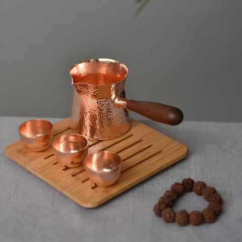 Copper Teapot With Wooden Handle Dope Hammered Turkish Coffee Pot on wooden tray, three cups beside, handcrafted in Turkey.