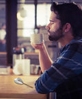 Man enjoying coffee, Ceramic Spoon Rest and Stainless Steel Stirrer Holder for Coffee and Tea Spoons on countertop in cafe.