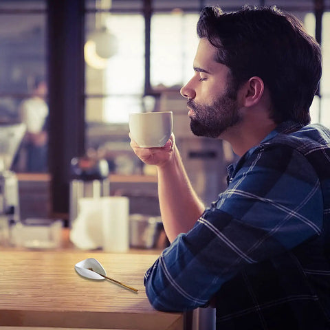 Man enjoying coffee, Ceramic Spoon Rest and Stainless Steel Stirrer Holder for Coffee and Tea Spoons on countertop in cafe.