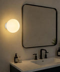 Minimalist Globe Wall Sconce, 1-Light White E27 Round Wall Light Fixture glowing beside a modern bathroom mirror.