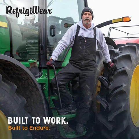 Man wearing Extreme Cold Insulated Bib Overalls For Men And Women, Tough As Nails Waterproof Wind Resistant Snow Coveralls With 400 Plus Grams Of Warmth, Heavy Duty Winter Work Gear, Black And Lime, XXL, standing on a tractor.