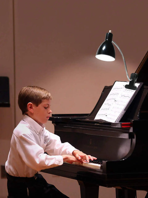 Boy playing piano with eye-caring clip on desk lamp with 360 degree gooseneck reading light attached to music stand