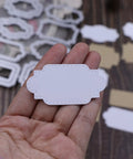 White ornate label-shaped scrapbooking cut-out from a metal cutting die, stitched-edge detail, held in hand