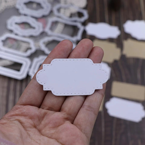 White ornate label-shaped scrapbooking cut-out from a metal cutting die, stitched-edge detail, held in hand