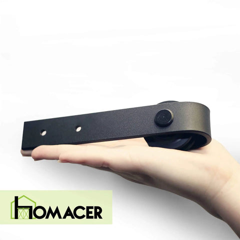 Close-up of a hand holding a component from the Mini Black Rustic Sliding Barn Door Hardware Kit For Two Doors 54 Inch Flat Track Non Bypass With Classic Roller Design Ideal For TV Stand Cabinet Vanity And Console Use.