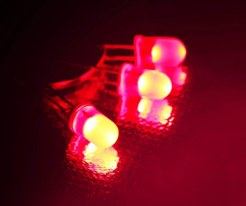 Hella Bright 5mm LED Diodes 100 Pack, diffused round bulbs glowing with a vibrant red hue on a reflective surface.