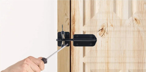 Person using a screwdriver to install a Heavy-Duty Silicone Automatic Gate Latch 7.4 Inch on a wooden door.