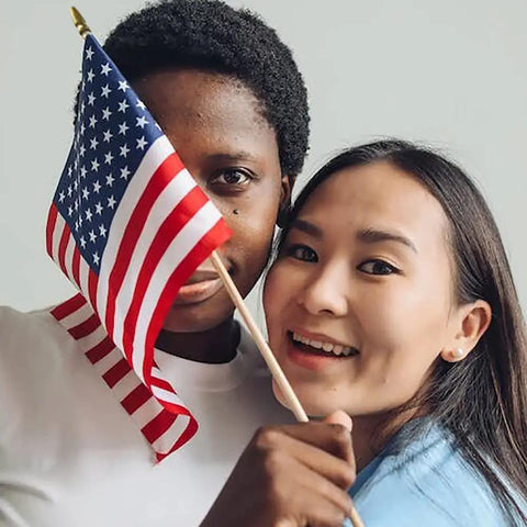 Two people holding a handheld flag from the 12 Pack 8x12 Inch American Flags on Sticks for Outdoor Use with Grounded Multi Purpose Flagpole Handheld Flags