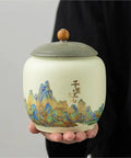 Top Shelf Ceramic Tea Tin With Woven Rattan Travel Case, Stunning Mountain Landscape Design, Go To Stash Jar For Loose Leaf Tea Or Specialty Coffee Beans In Slate Blue, held in hand.