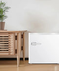 Mini Upright Freezer 1.2 Cu Ft Compact Build With Removable Slides And Adjustable Thermostat Dial In Bright White Finish next to a wooden table.