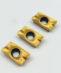 Close-up of three carbide inserts for CNC milling and turning tools APMT1604PDER, multilayer coated for hard steel machining.
