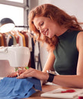 Front view of a white sewing machine stitching blue fabric, worn by a woman in a green sleeveless top.