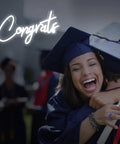 White Congrats Neon Sign Dimmable LED Wall Art For Graduation Party And Wedding Backdrop glowing beside graduates hugging