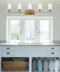 Cool Five Light Brushed Brass Vanity Light Fixture With Clear Glass Shades Mounted Above Bathroom Sink
