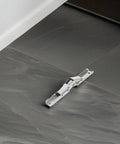 Close-up of space saving corner cabinet hinges with short arm wide angle design in cold rolled steel on gray tile floor.