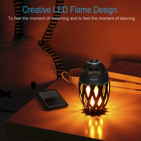 LED Flame Outdoor Table Lamp With Bluetooth Speaker on table, emitting warm light in dark room setting.