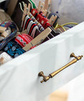 Drawer with Six Pack 5 Inch Antique Brass Cabinet Pulls, showing ornate handles and decorative finials in a vintage setting.
