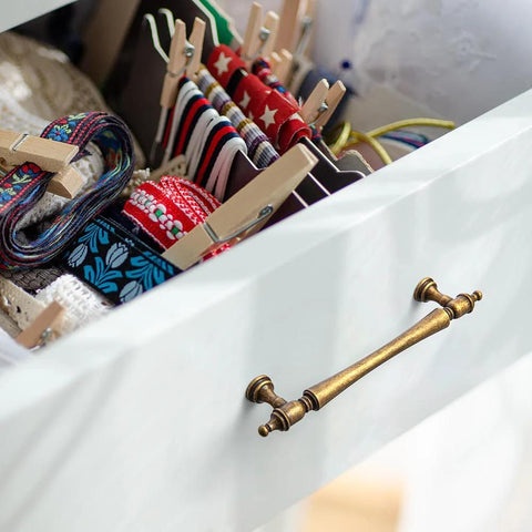 Drawer with Six Pack 5 Inch Antique Brass Cabinet Pulls, showing ornate handles and decorative finials in a vintage setting.