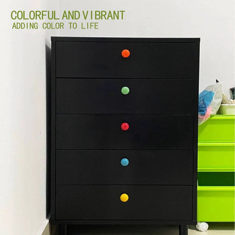 Black dresser with colorful knobs next to a green cabinet and a variety of colorful items on top.