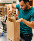 Man placing baguette in Heavy Duty Kraft Paper Bags With Handles 10 x 7 x 12 Inches, 250 Pack Brown Shopping Bags For Grocery