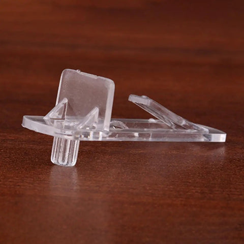 Close-up of a clear plastic shelf support clip with locking pin on a wooden surface, part of 30 Pack Plastic Shelf Support Clips Locking Pins For Cabinets Furniture Shelving Brackets Transparent Reusable Pegs For Kitchen Bookcase Garage Storage.