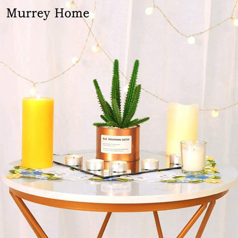 Decorative table setup with yellow candles, faux cactus in pot, and string lights creating a cozy ambiance.