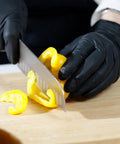 Person wearing black gloves slicing yellow bell pepper on cutting board