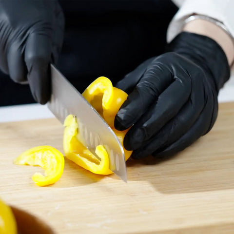 Person wearing black gloves slicing yellow bell pepper on cutting board