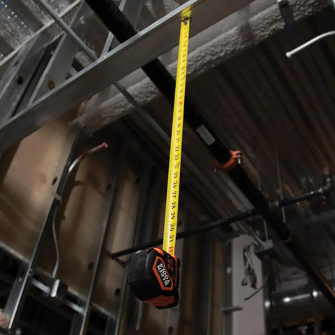 Heavy-Duty Tape Measure With Nylon-Coated Blade, 25-Foot Reach in use at a construction site, measuring overhead distance.