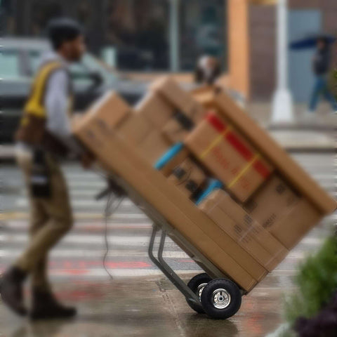 Person using hand truck with 4 Pack 10 Inch Tough As Nails Replacement Tire And Wheel For 4.10/3.50-4 on a rainy street.