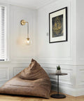 Mid Century Modern Wall Light With Adjustable Cord Raw Brass Round Glass Sconce And Amber Lampshade in a cozy living room corner.