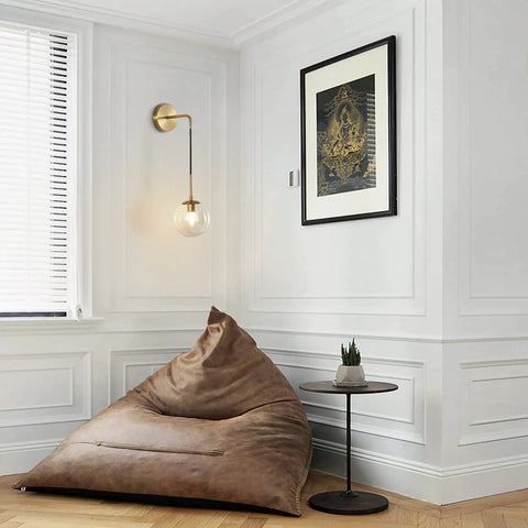Mid Century Modern Wall Light With Adjustable Cord Raw Brass Round Glass Sconce And Amber Lampshade in a cozy living room corner.