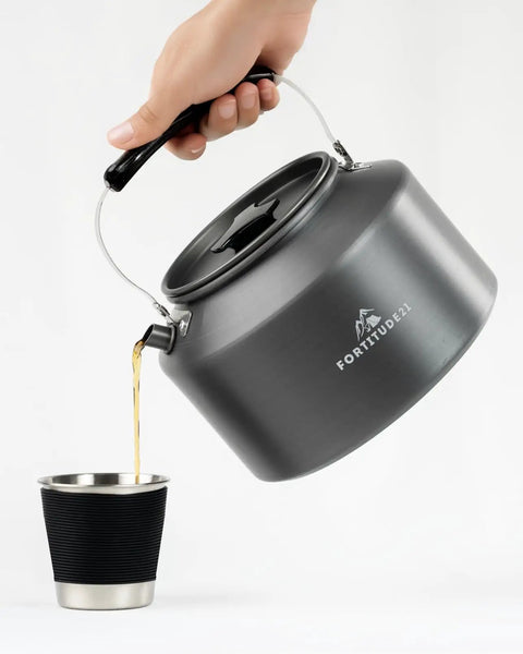 Pouring water from black Stovetop Camping Kettle 2.2 Liter Teapot for Boiling Water and Tea Brewing into cup, outdoor use