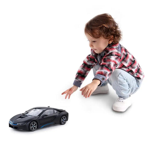 Child playing with BMW I8 1:14 Scale Remote Control Car With Open Scissor Doors, Matte Black RC Toy Vehicle on a white background.