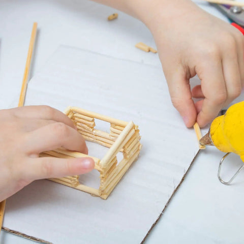 Child assembling a model house with Premium Unfinished Birch Dowel Rods 1/4 X 6 In Natural Hardwood Sticks for Crafts.