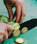 Crinkle cutter, black plastic blade, close-up of slicing cucumber by hand on green cutting surface