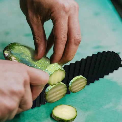 Crinkle cutter, black plastic blade, close-up of slicing cucumber by hand on green cutting surface