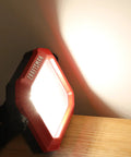 Beast Bright 1100 Lumen 4000K LED Tiltable Portable Work Light on wooden surface, illuminating wall with impact-resistant glass lens.