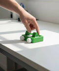 Hand holding a green plastic toy car on a white surface, unrelated to Portable Wire Soldering Fixture And Clamp Holder