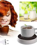 Woman holding a steaming cup of coffee next to a cup warmer with milk jug and glass in background.